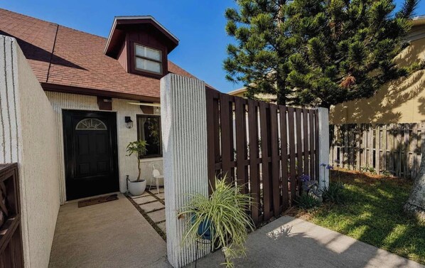A residential property with a front door, a small porch, a wooden fence, and a pine tree.