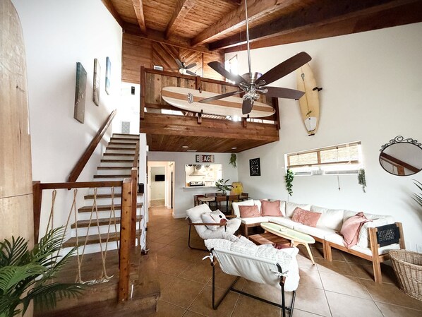 A spacious living area with a high ceiling, a ceiling fan, and a surfboard decoration.