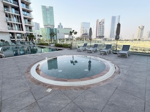 A rooftop pool area with lounge chairs and a city skyline view. - Luxury Waterfront 1BR Steps to Cleveland, Galleria and ADGM By Betu (Abu Dhabi)