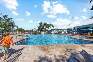 A swimming pool with a tiled deck, lounge chairs, and umbrellas. - Condo 2BR en Windsor Palms cerca de Disney (Kissimmee)