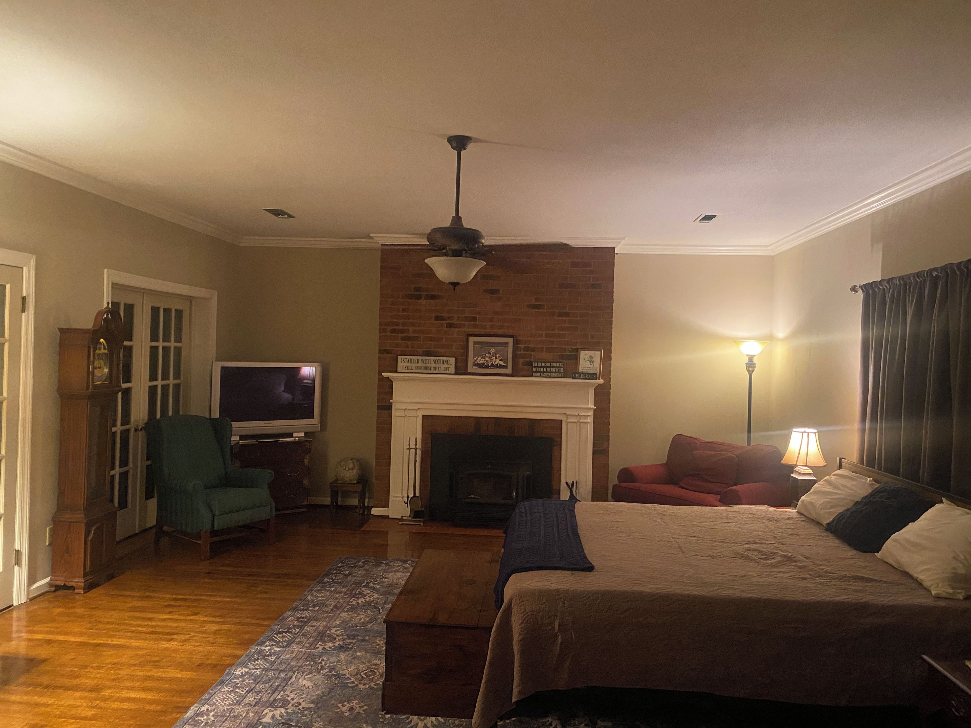 A bedroom with a fireplace, a television, a bed, and a desk with a lamp.