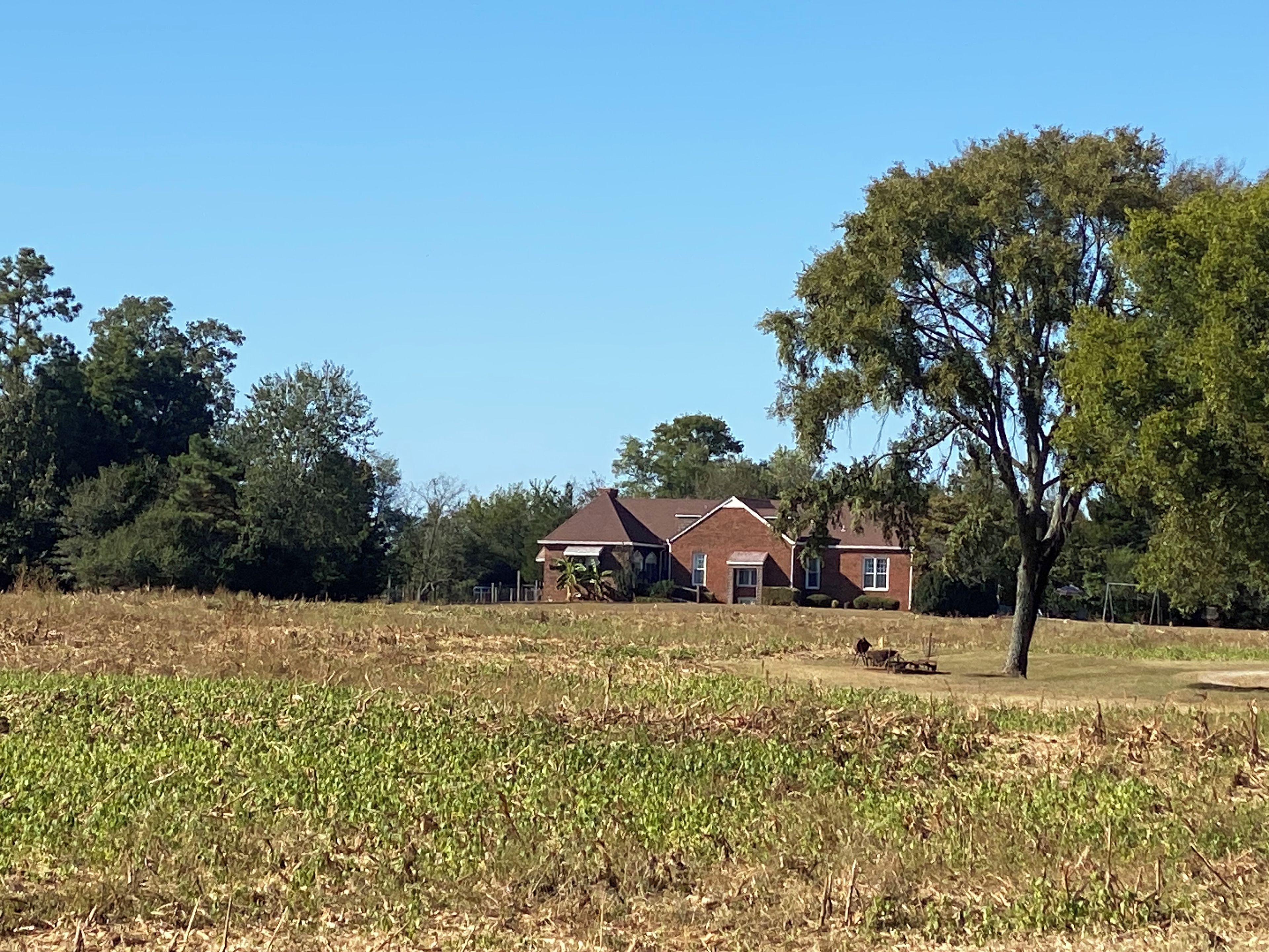 A two-story house with a red roof, surrounded by a field and trees.