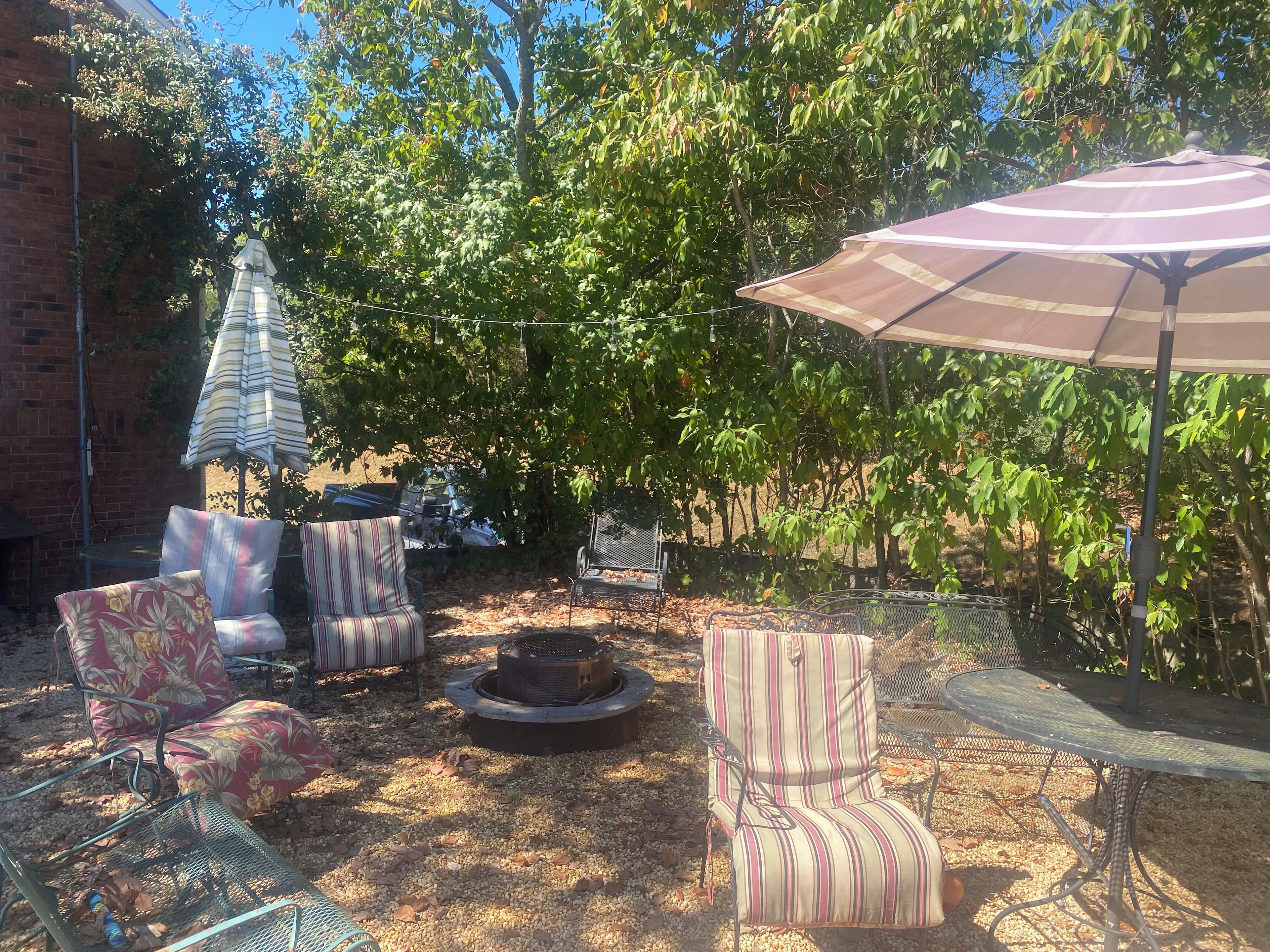 An outdoor seating area with chairs and a table, surrounded by trees and a brick wall.