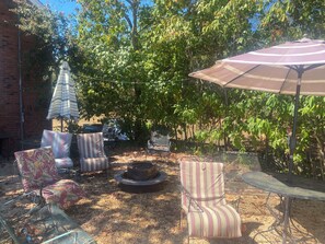 An outdoor seating area with chairs and a table, surrounded by trees and a brick wall.