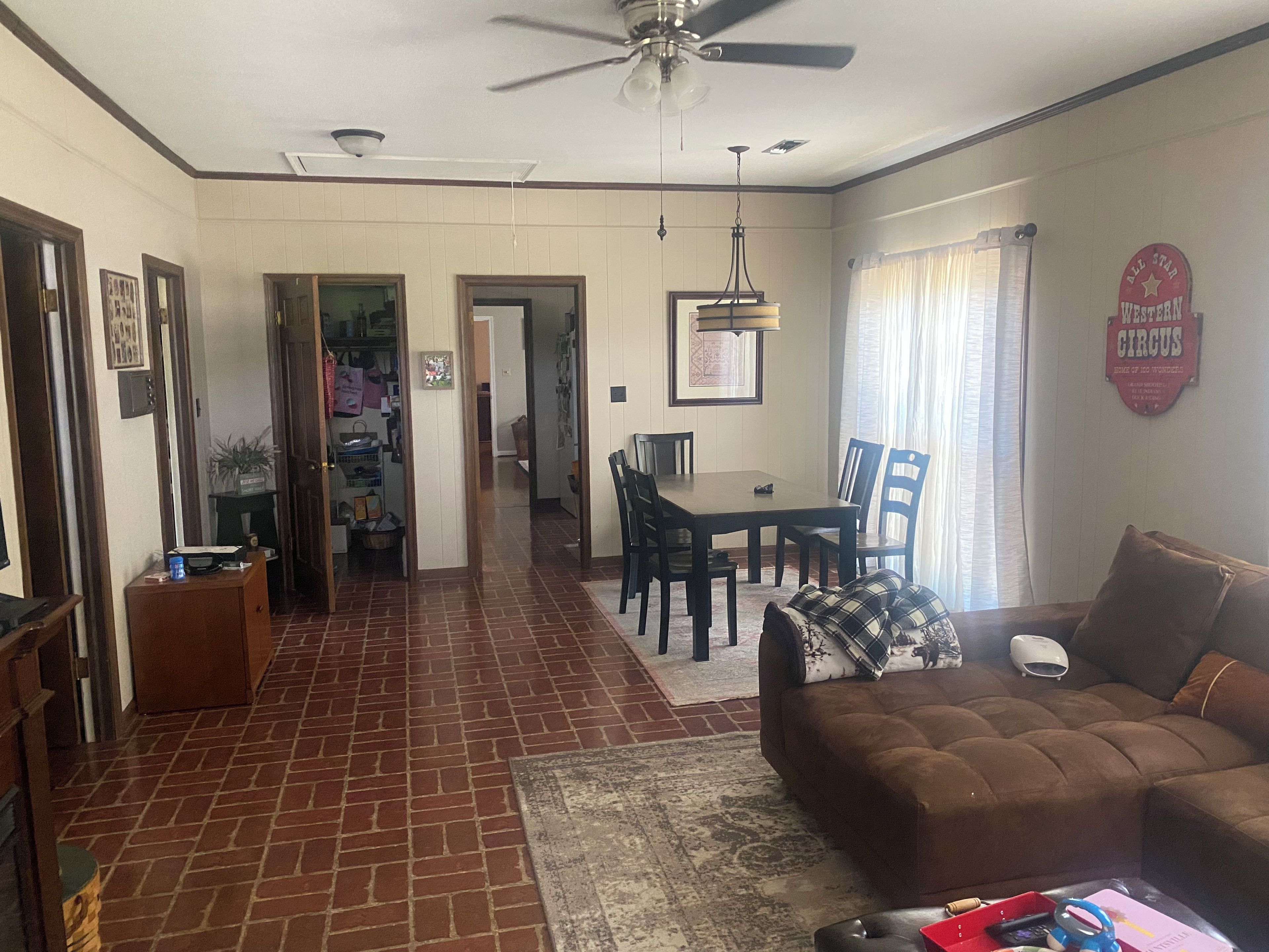 A living room with a brown sofa, a dining table with chairs, a ceiling fan, and a rug.