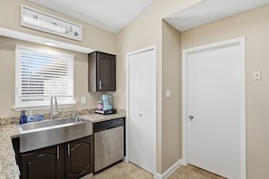 A compact kitchen with a built-in dishwasher, a window with blinds, a door, and a countertop with a coffee maker. - Family Friendly, Near The Lake, Games, BBQ, More (The Colony)