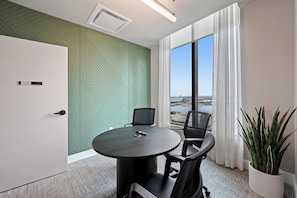 A conference room with a round table, two chairs, a potted plant, and a view of a body of water through large windows. - 501 First Loft Balcony by Palermo Home (Miami)