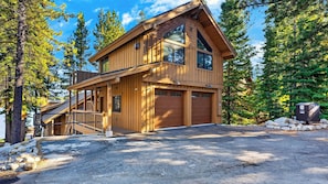 A two-story wooden cabin with a garage, surrounded by trees.