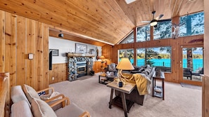 A cozy cabin interior with a stone fireplace, wooden walls, a sofa, and a view of a lake. - Meeks Bay Chalet by Avantstay Lakefront Retreat Boat Dock + Hot Tub Near Beach (Tahoma)