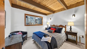 A bedroom with a bed, a desk, a chair, a window, and a wooden ceiling.