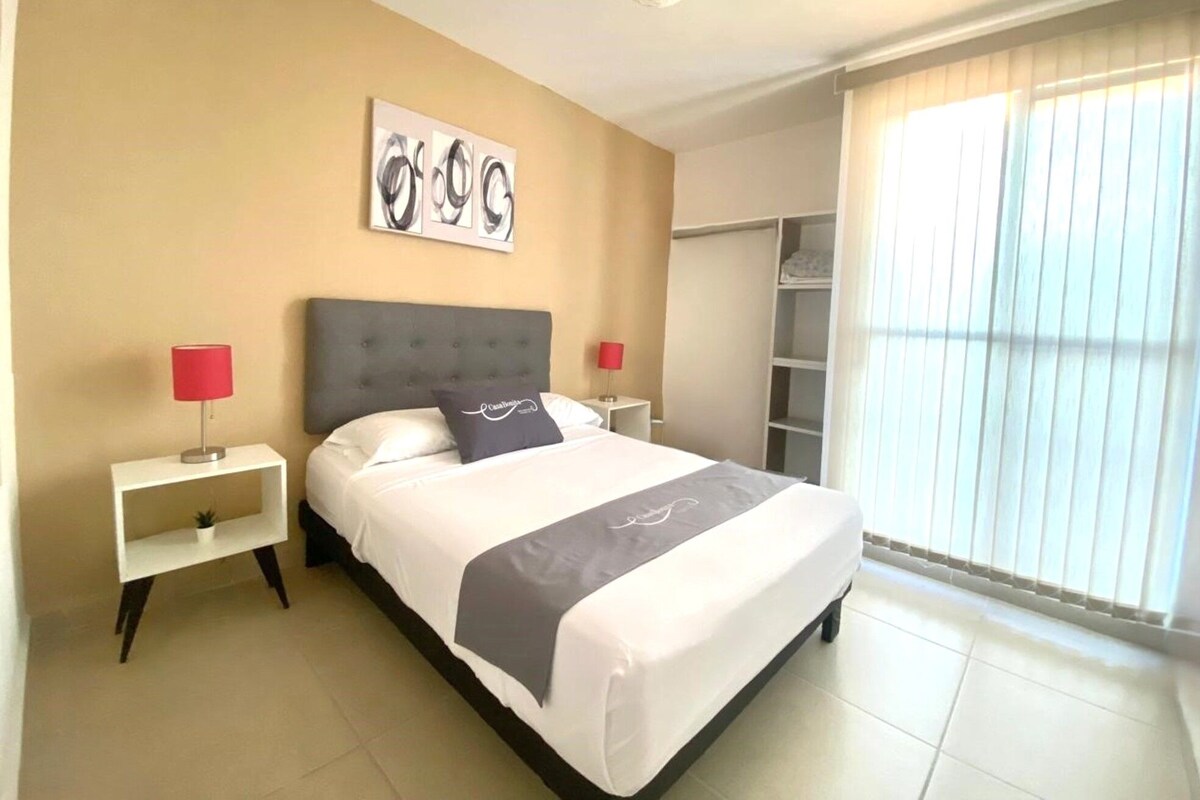 A hotel room with a bed, two bedside tables, a nightstand, a wardrobe, and a window with blinds.