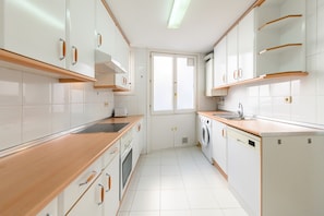 Eine moderne Küche mit weißen Schränken, Holzarbeitsplatten, einem eingebauten Ofen, einer Waschmaschine und einem Fenster für natürliches Licht.