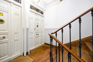 Eine Treppe mit Holzhandlauf und schwarzen Spindeln, die zu einer weißen Tür mit Messingknauf und einem dekorativen Metallgitter führt.