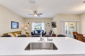 A modern kitchen with a central island, a dining area with chairs, a sofa, and a ceiling fan. - Family Townhouse Near Disney | HeatedPool | Lazy River (Kissimmee)
