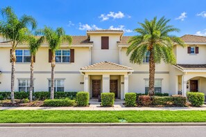 A multi-story residential building with a symmetrical facade, a central entrance with a covered porch, and a clear blue sky. - Family Townhouse Near Disney | HeatedPool | Lazy River (Kissimmee)
