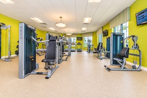 A gym with various exercise machines, a bright yellow wall, and a large window providing natural light. - Family Townhouse Near Disney | HeatedPool | Lazy River (Kissimmee)