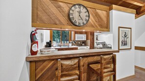 A kitchen with a wooden bar, a large clock, and a fire extinguisher. - Northstar Pines by Avantstay Pine-view Deck Shared Pool + Spa Steps to Northstar Shuttle (Truckee)