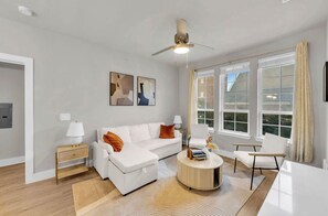 Een moderne woonkamer met een witte bank, een ronde salontafel en een plafondventilator.
