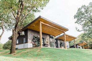 Ein modernes Haus mit großer Veranda, bodentiefen Fenstern und einem Baum im Vordergrund.