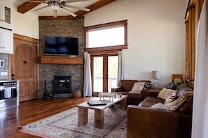 A living room with a stone fireplace, a television mounted above it, and a large window. - The Cabin With The OK View (Grayson County)