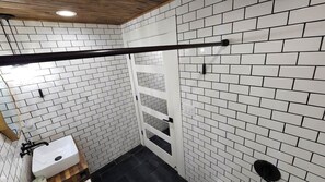 Ein Badezimmer mit weiß gefliesten Wänden, einer Holzbalkendecke, einem weißen Waschbecken und einer schwarzen Rohrleitung.
