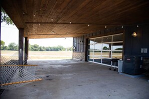 Un'area esterna riparata con pavimento in cemento, un'amaca, un'ampia porta garage e un condizionatore metallico.