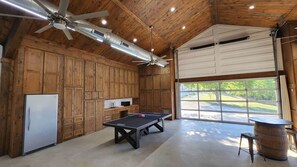 Un'ampia stanza con tavolo da ping pong, mobili in legno, ventilatore a soffitto e un'ampia finestra che offre vista sull'esterno.