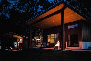 Ein modernes Haus mit überdachter Veranda, großen Fenstern und einem Feuerbereich.