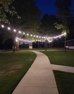 A pathway leading to a building with string lights overhead. - Texas Tiny Cabins #2 – Peaceful Cabin, Scenic View (Grayson County)