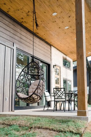 Un espacio al aire libre moderno con un sillón colgante, una mesa y sillas.