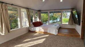 Una camera da letto con un letto grande, diverse finestre e vista sugli alberi.