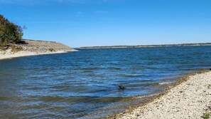 Ruhige Wasserfläche mit Kiesufer und einer fernen Küste.