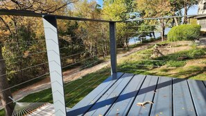 Eine Holzterrasse mit Metallgeländer, die auf einen Garten und ein Gewässer blickt.