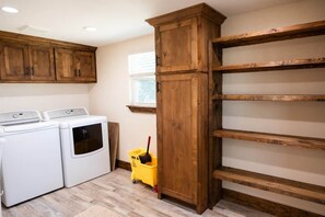 Ein Waschraum mit zwei weißen Waschmaschinen, einem Holzschrank und einem gelben Reinigungswagen.