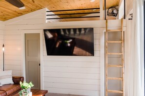 Ein Wohnzimmer mit einem großen Flachbildfernseher an einer weißen Wand, einer Holzbalkendecke und einem braunen Ledersofa.