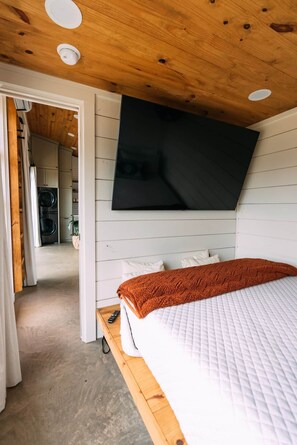 Een slaapkamer met een bed, een wandtelevisie en een zichtbare wasruimte.