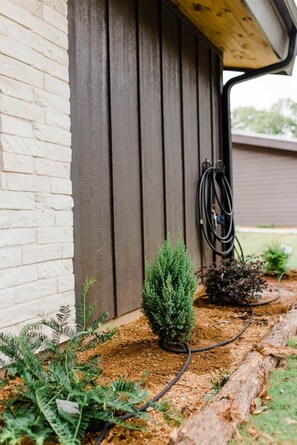 Ein Gartenbereich mit einem kleinen Baum, einem Gartenschlauch und einer Holzterrasse.