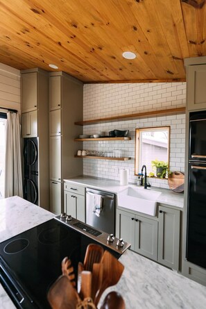 Een moderne keuken met een centraal eiland, een houten plafond en een witte betegelde achterwand.