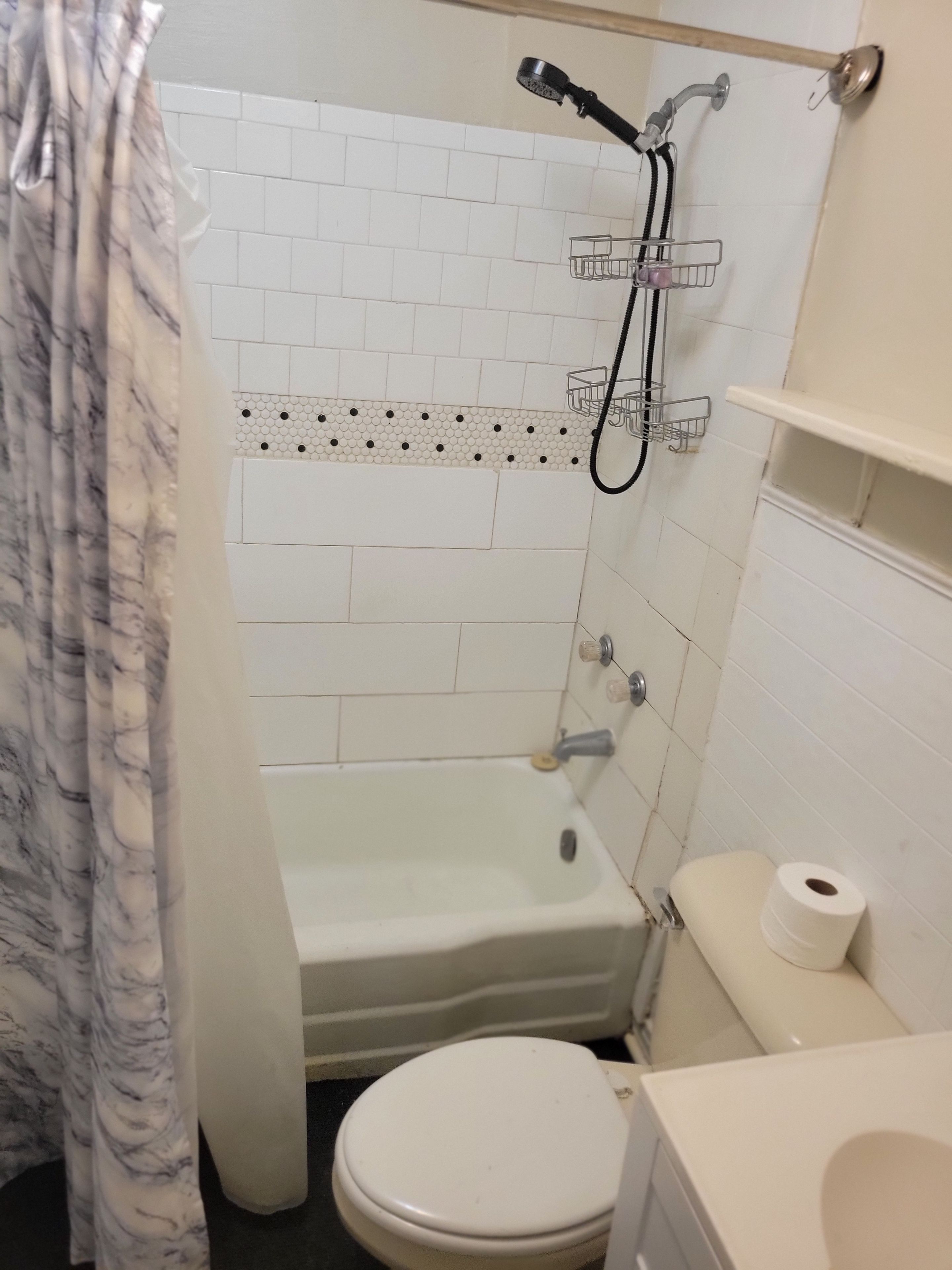 A bathroom with a white bathtub, a toilet, and a shower head.