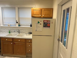 Una cocina con armarios de madera, un refrigerador blanco, un lavamanos y una ventana con persianas.