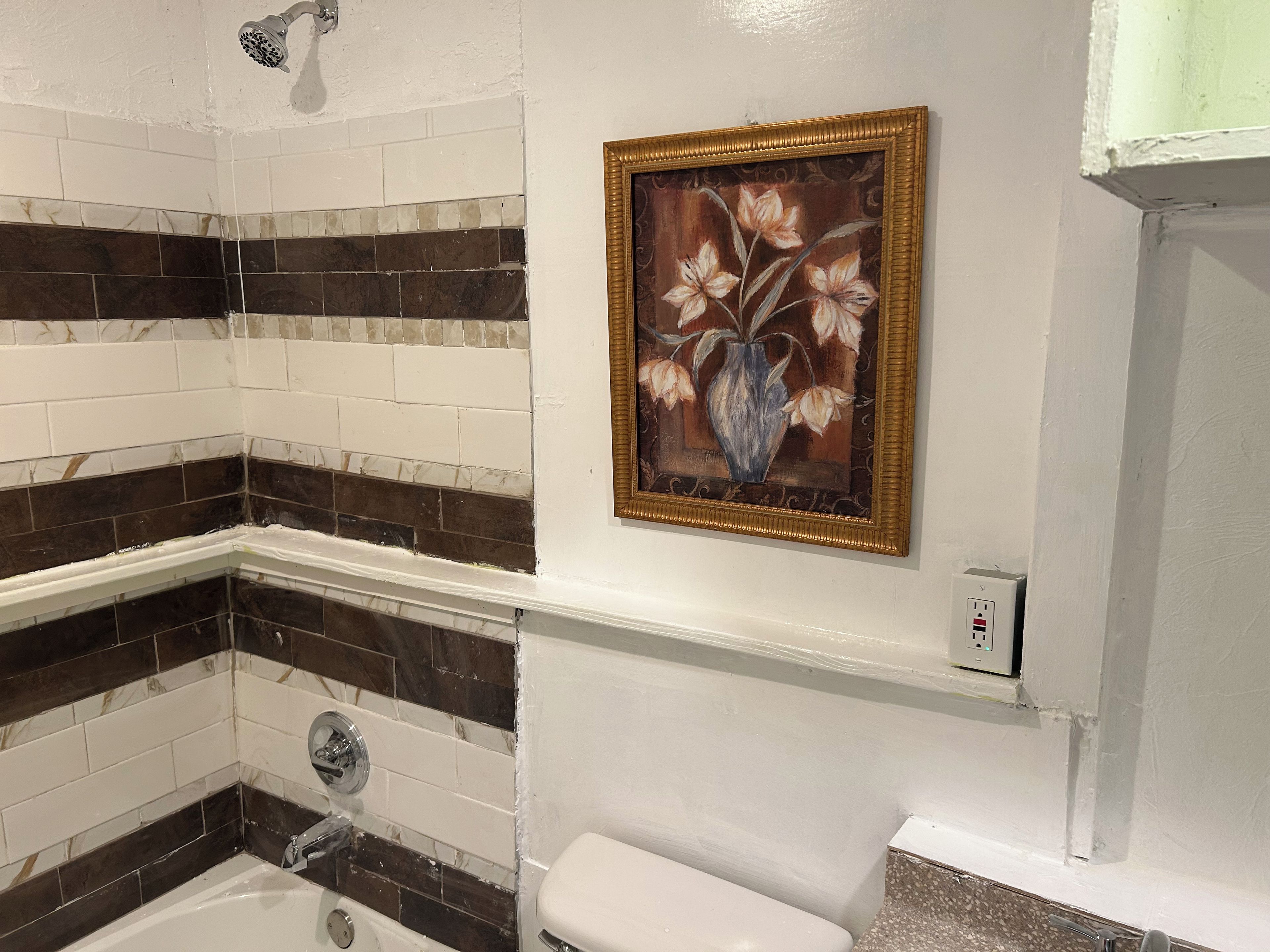 A bathroom with a white toilet, a bathtub with a showerhead, and a wall-mounted painting of flowers.