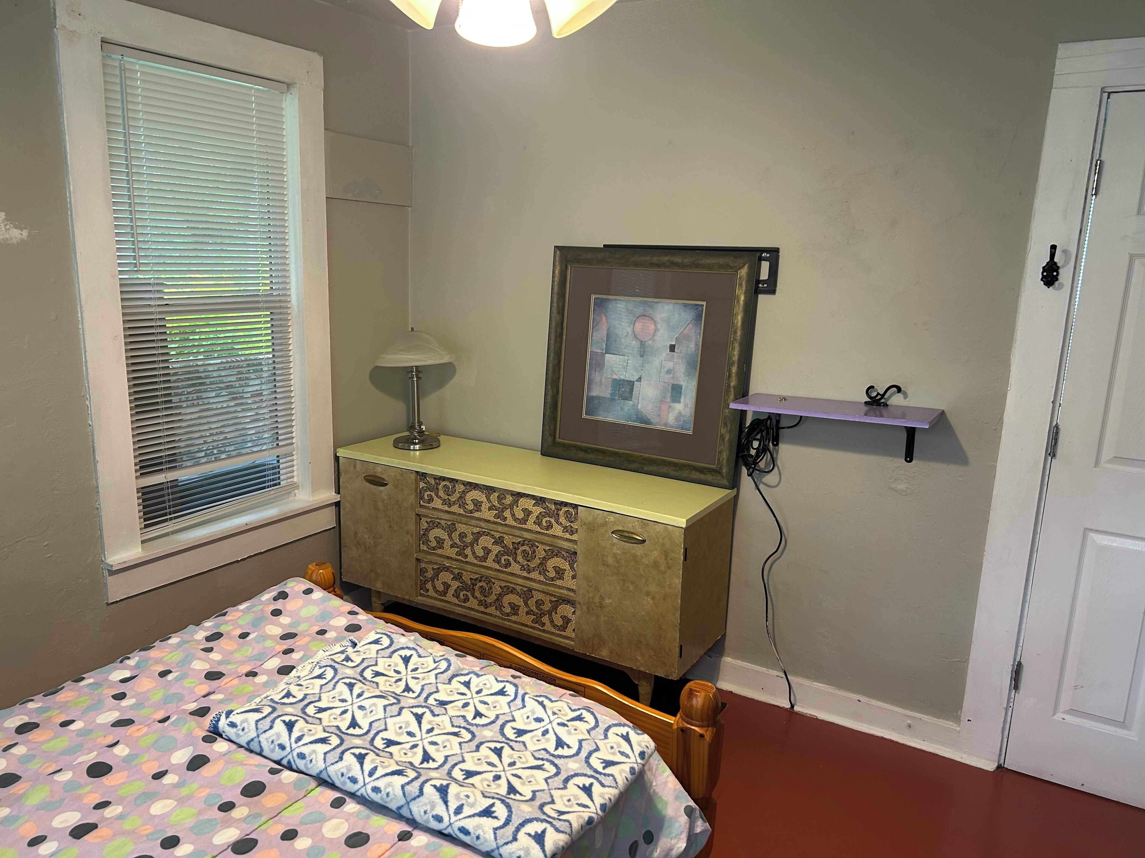 A bedroom with a bed, a dresser, a lamp, a picture frame, and a door.
