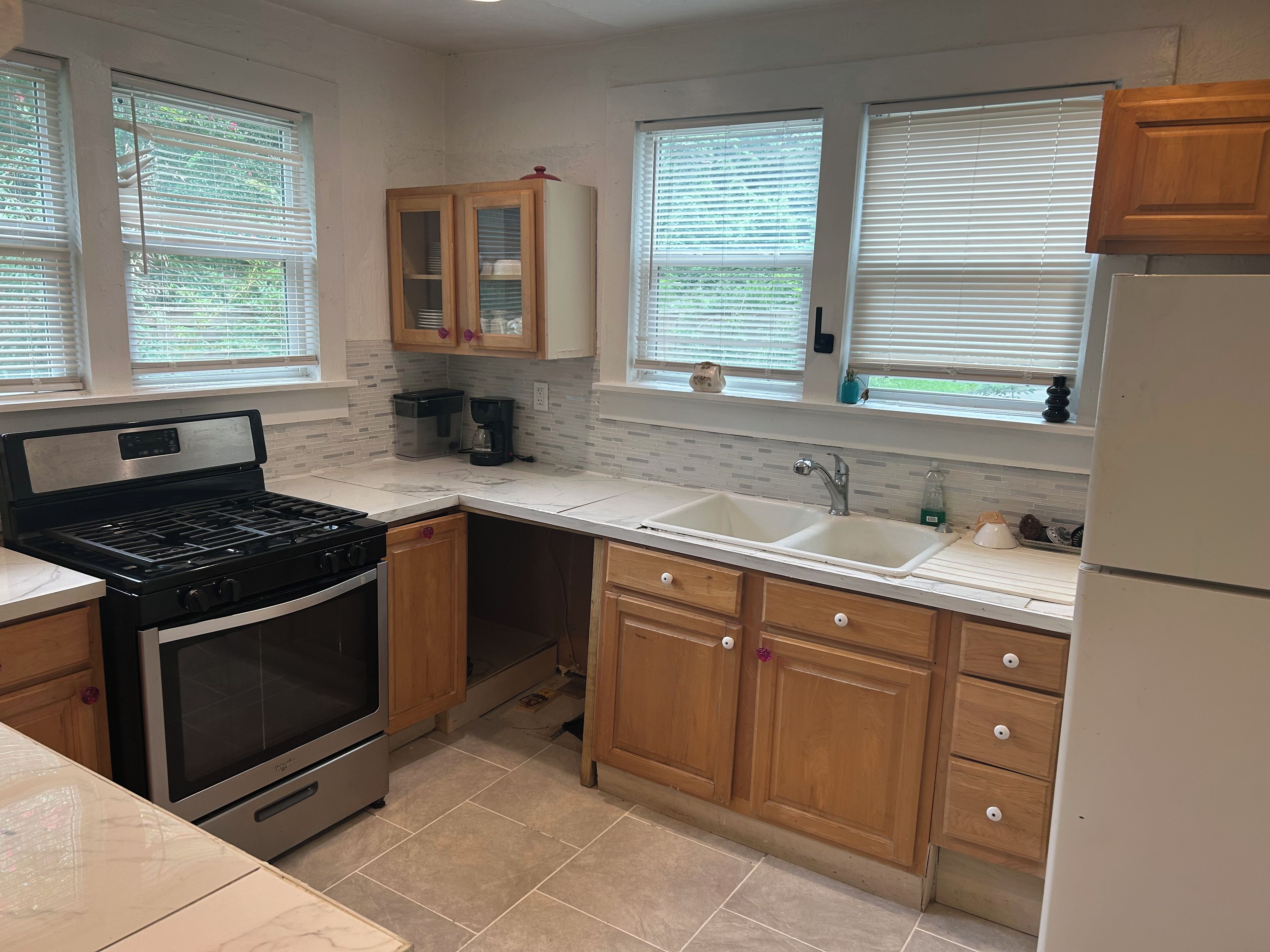 A kitchen with a stove, sink, cabinets, and a window with blinds.