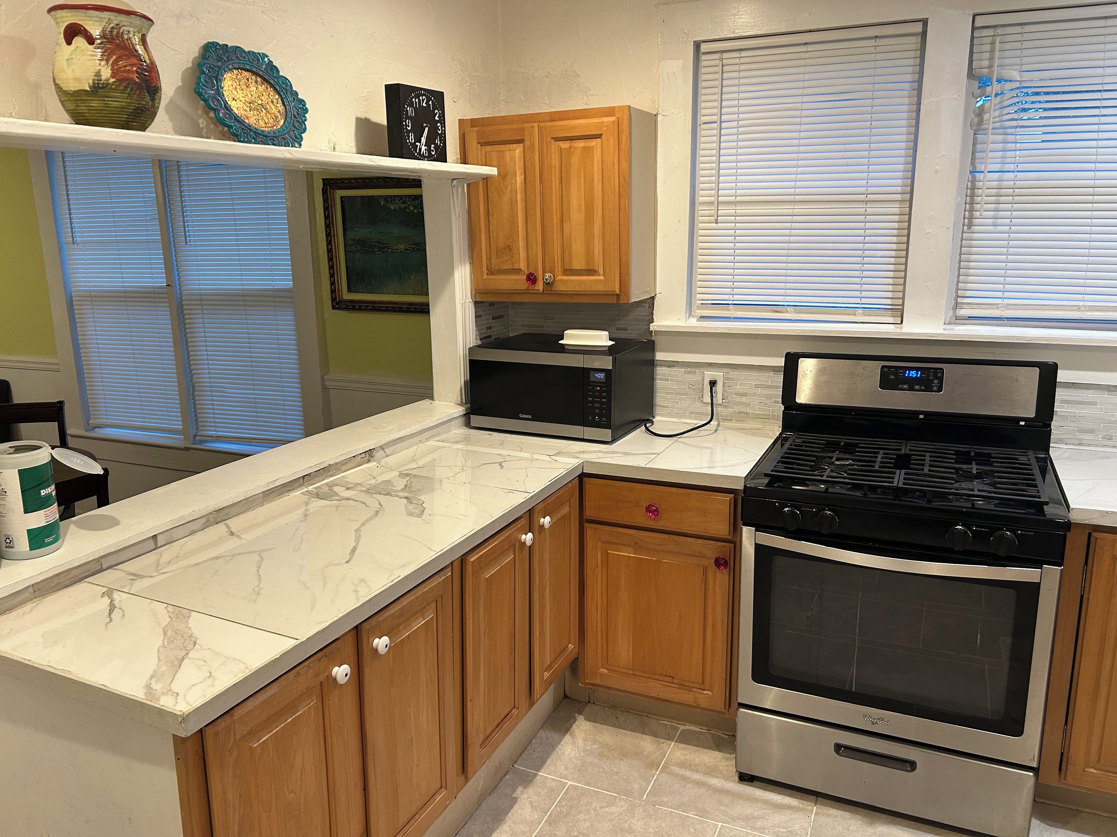 A kitchen with wooden cabinets, a microwave, a stove, and a window with blinds.
