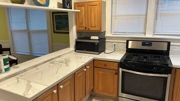 A kitchen with wooden cabinets, a microwave, a stove, and a window with blinds.