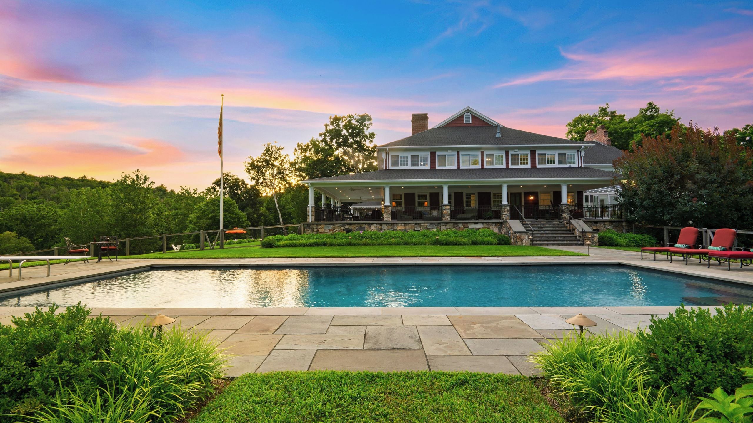 A two-story house with a swimming pool, a covered patio, and a flagpole.