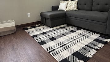 A living room with a sectional sofa, a patterned rug, a window, and a framed picture on the wall.