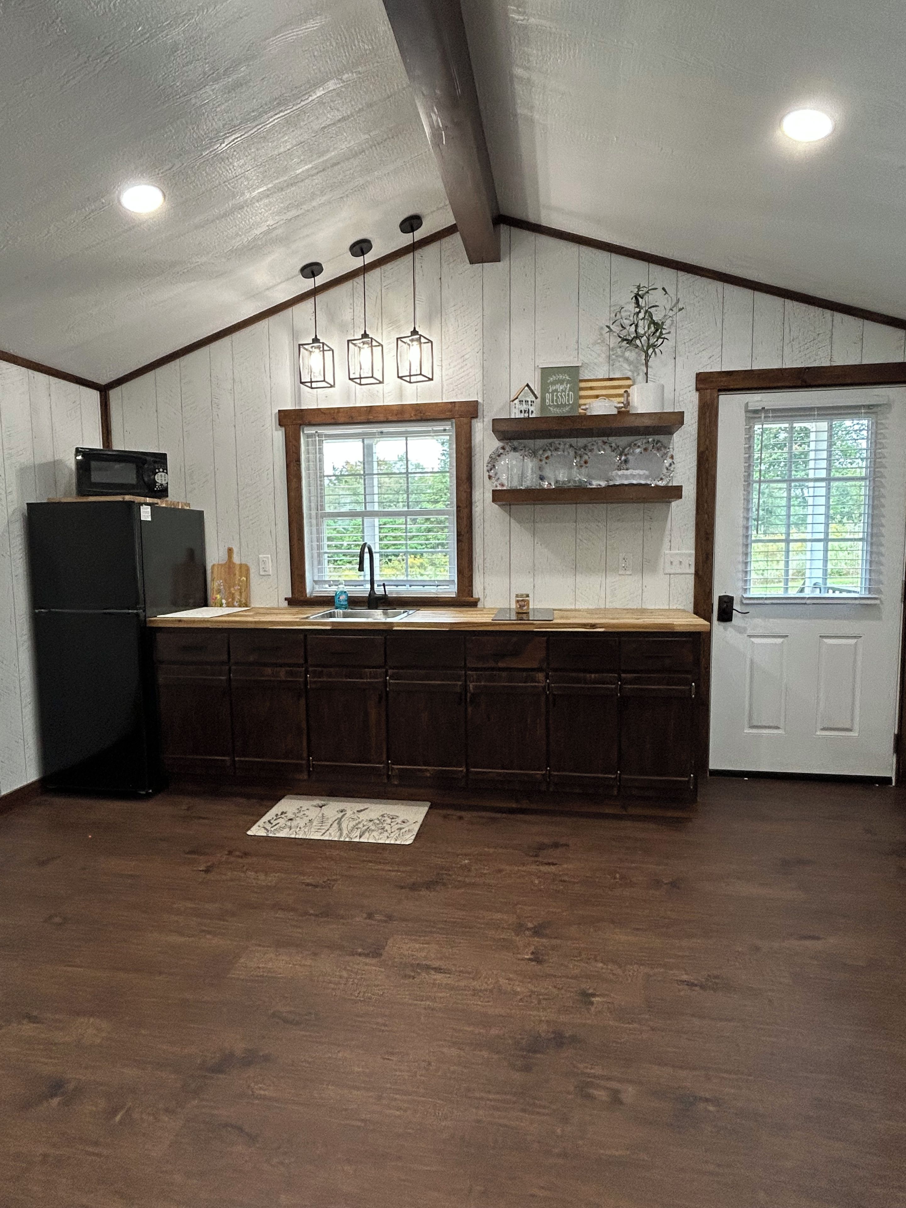 A kitchen with a wooden countertop, a black refrigerator, a sink, and a window with a view of greenery.