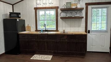 A kitchen with a wooden countertop, a black refrigerator, a sink, and a window with a view of greenery.