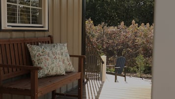 A wooden bench with a floral cushion, a chair, and a view of a garden with autumn foliage.